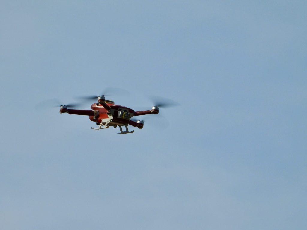 Red drone soaring high against sky.