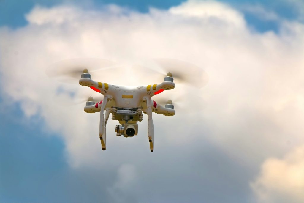 White drone flying through cloudy sky.
