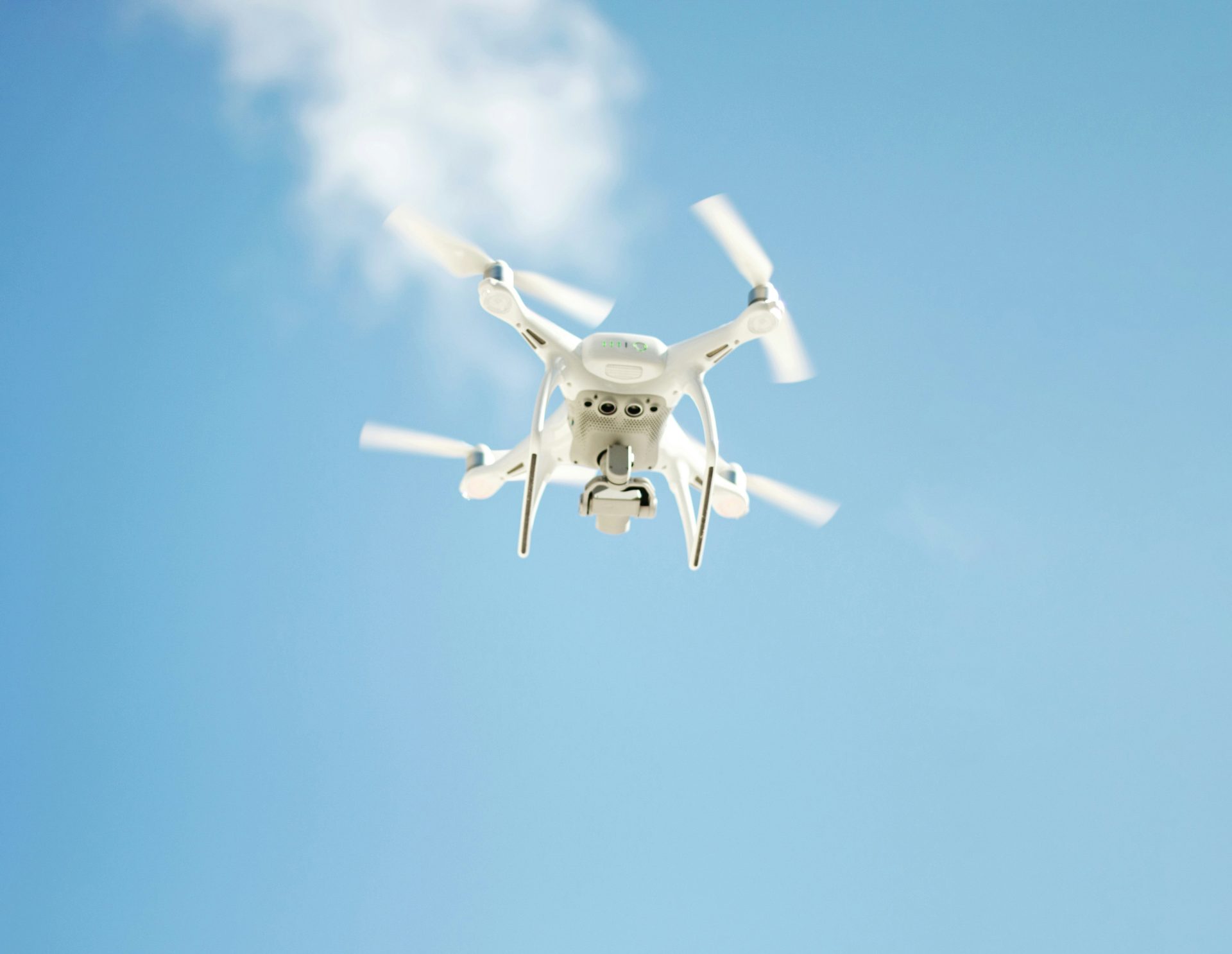 White drone flying under bright blue sky.